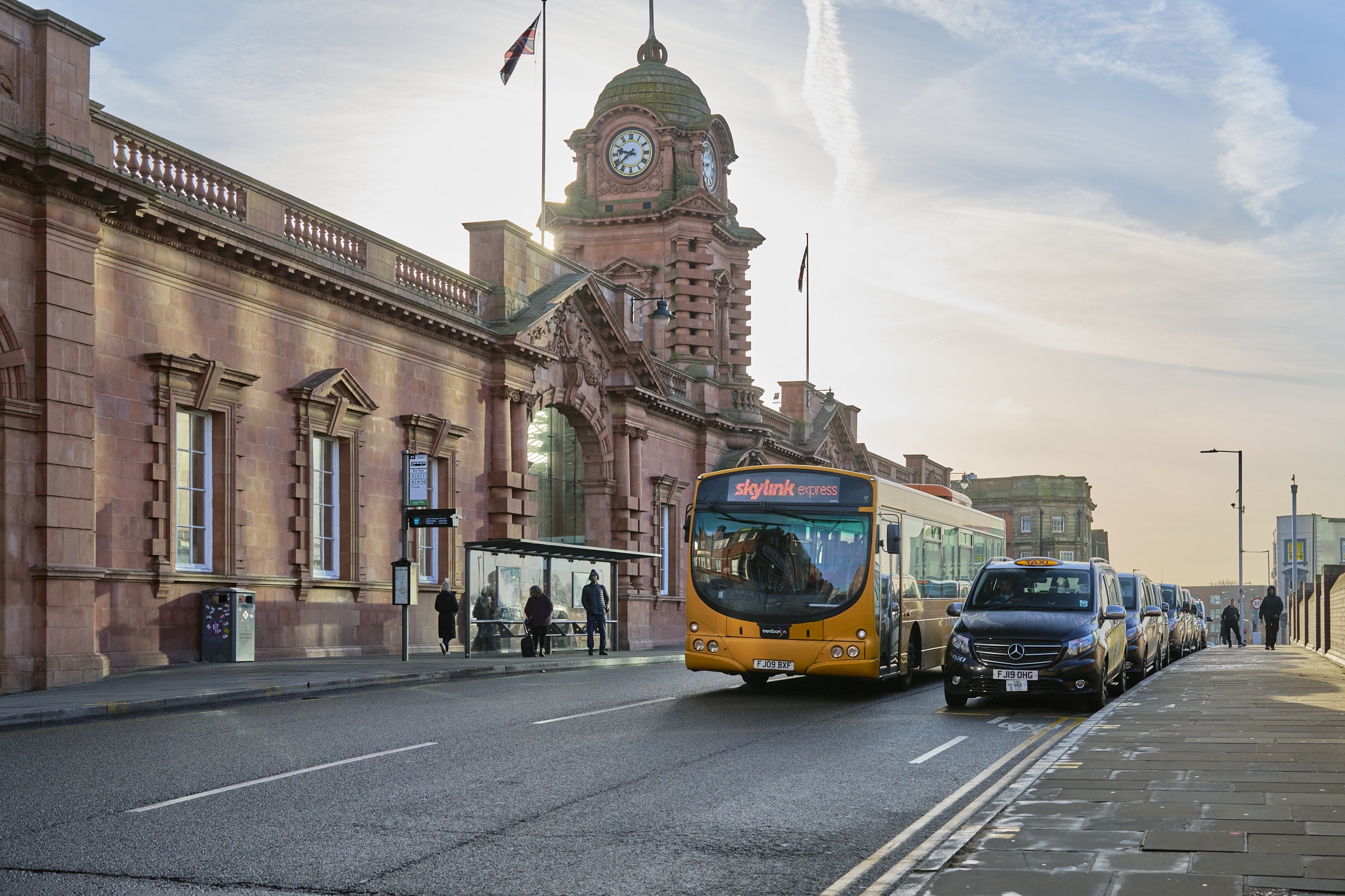 Transport: Outside of Nottingham train station. A bus and a row of taxis can be seen on the road.