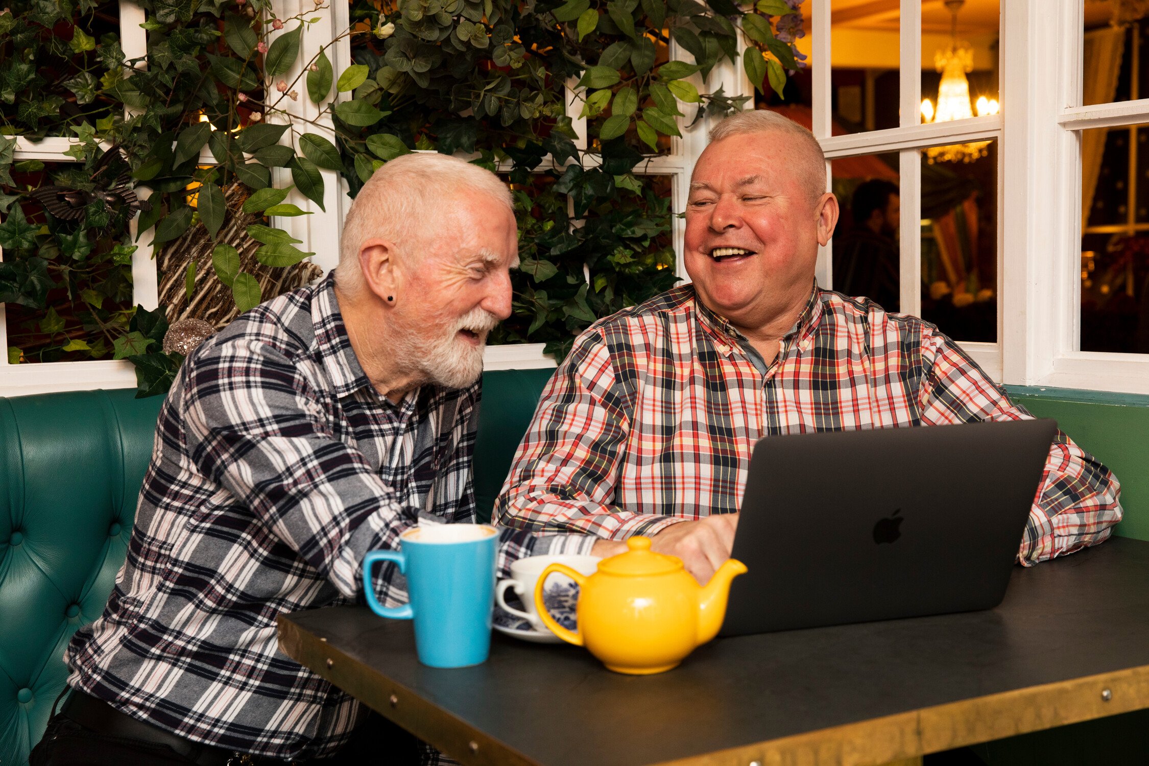 Two men are looking at a computer while having a cup of tea.