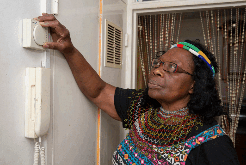A lady is at home, she is adjusting her thermostat.