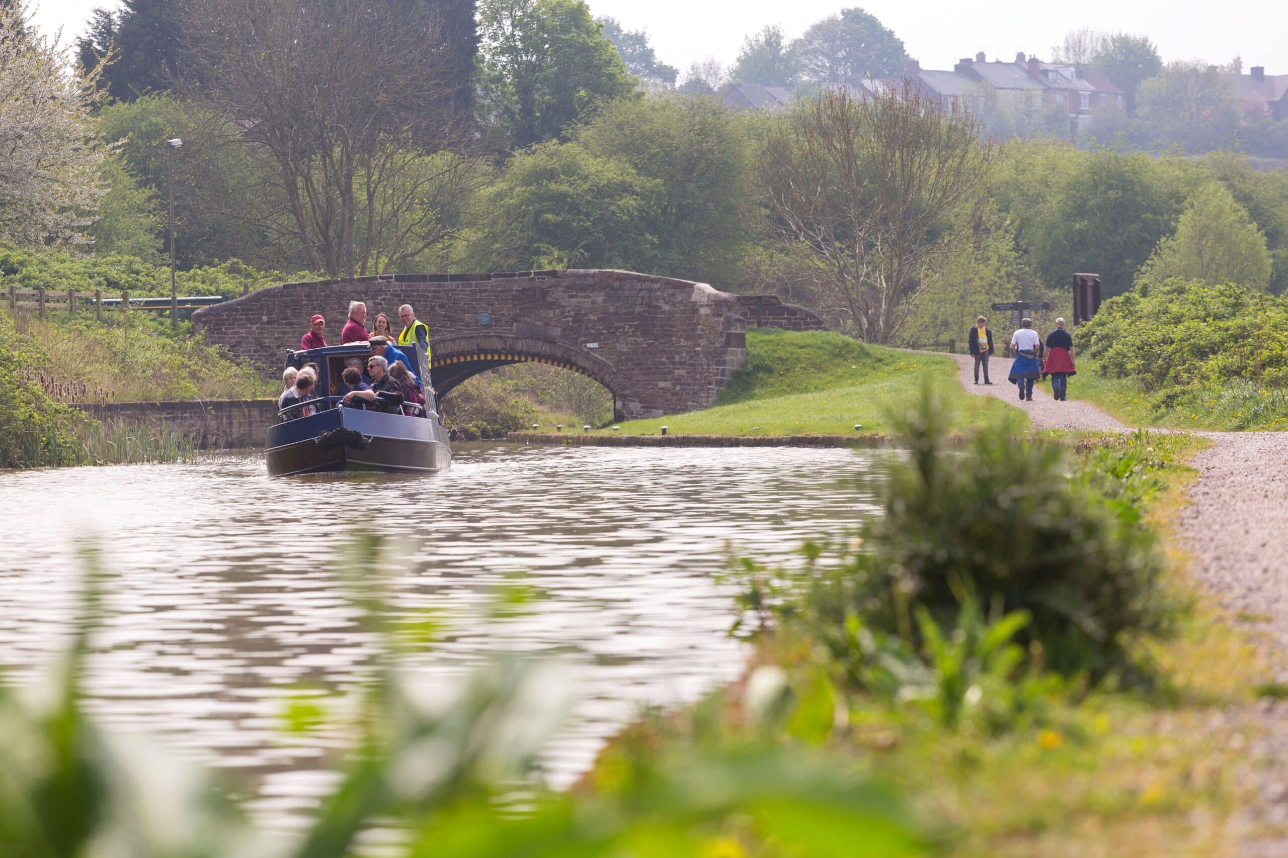 A canal boat travelling down the Chesterfield canal next to people walking along the tow path
