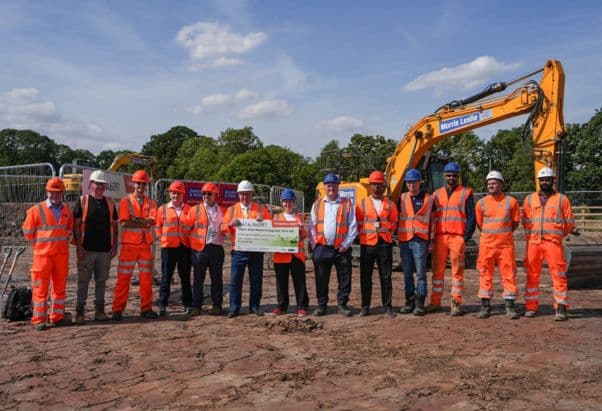 Mayor Claire at a614 Kirk Hill works stood with a group of construction workers in orange high vis, holding a a giant cheque in the middle